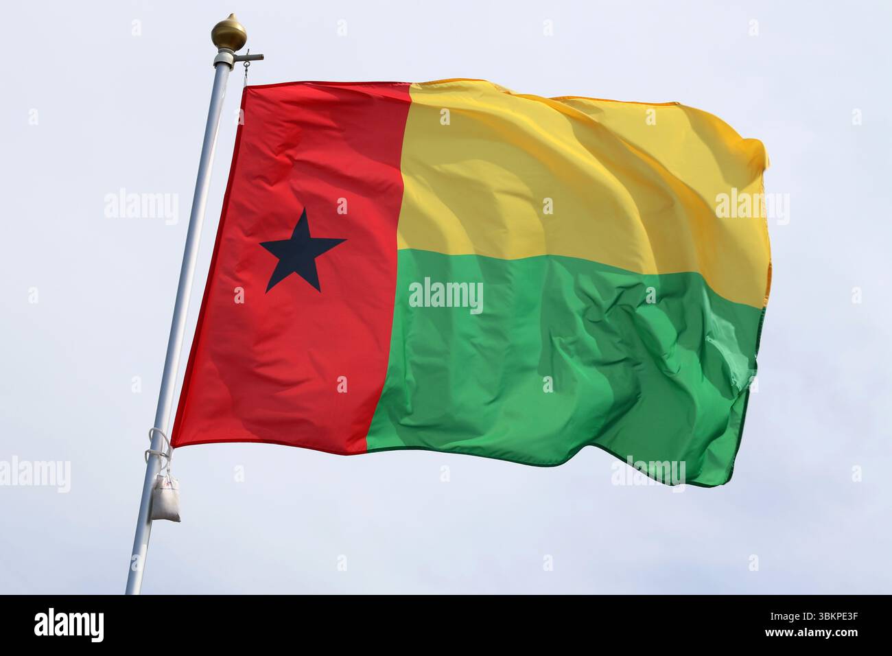 Die bissau-guineische Nationalflagge flattert im Wind an einem Fahnenmast. Stockfoto