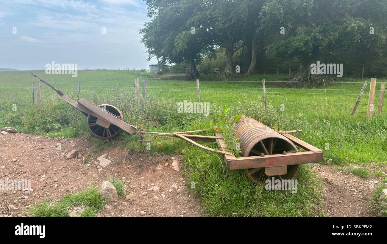 Rostige, verlassene Bauernwalzen ruhen in bewachsenem Gras, was verwittertes Metall und ländliche Verfall in der schottischen Landschaft zeigt. Stockfoto