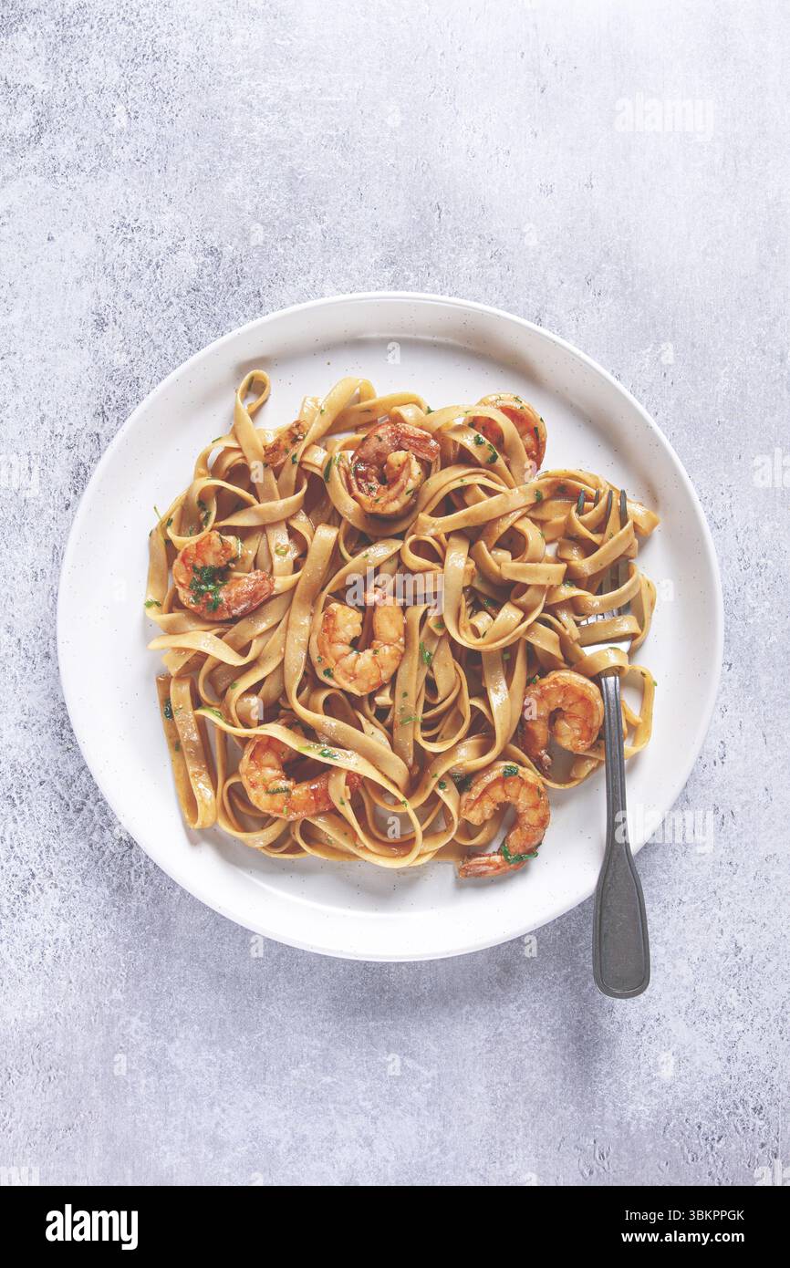 Fettuccine Nudeln mit Garnelen, scharf in Sojasauce, auf grauer Platte mit Gabel, Nahaufnahme Stockfoto
