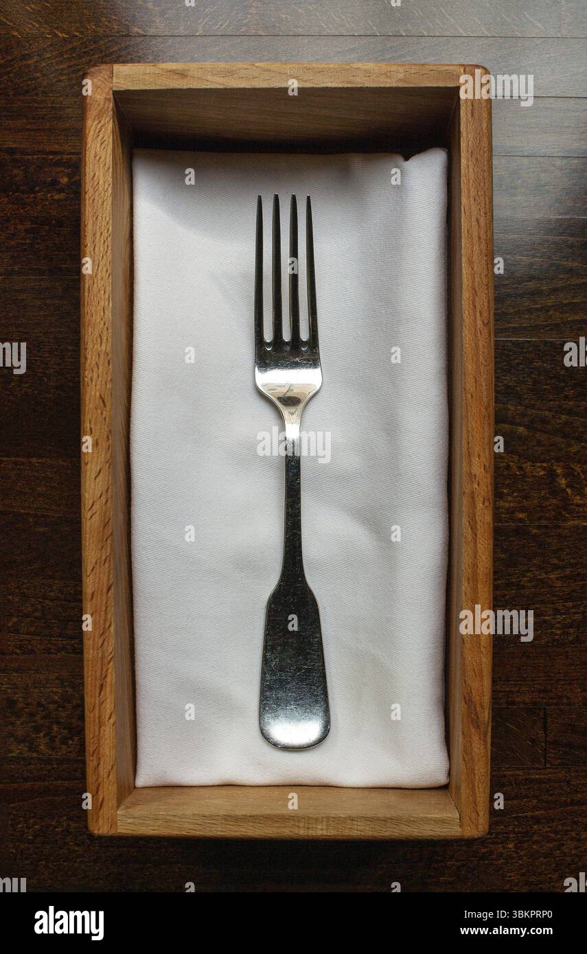 Eine antike Gabel liegt auf einer Baumwollserviette in einer Holzkiste, ein Fragment des Tischs in einem Restaurant Stockfoto