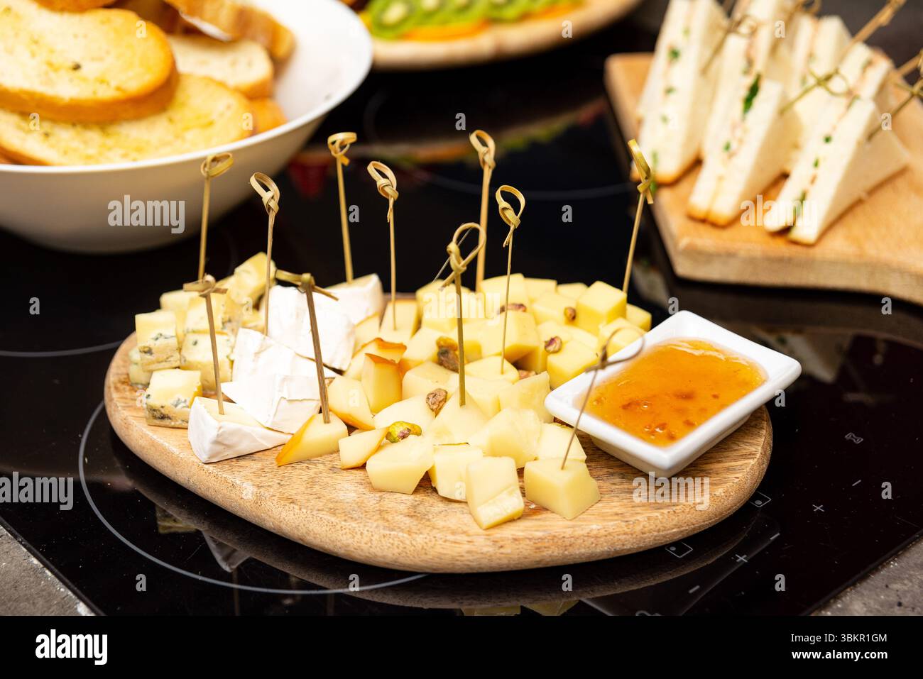 Elegantes Holzkäsebrett mit gemischten Käsewürfeln, Pistazien und Marmelade, perfekt für Wein oder Vorspeisen. Stockfoto