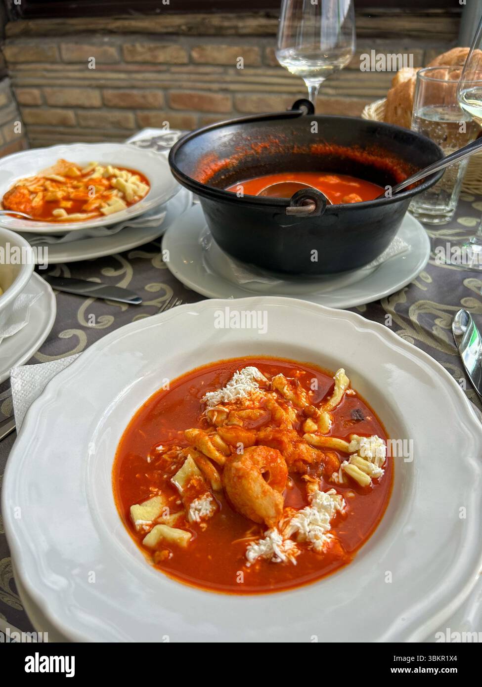 Köstlicher Roter Fisch-Eintopf mit Garnelen und handgemachter Pasta, serviert in einem rustikalen Ambiente mit Brot und Weißwein, die das Wesen des traditionellen Cui einfangen Stockfoto