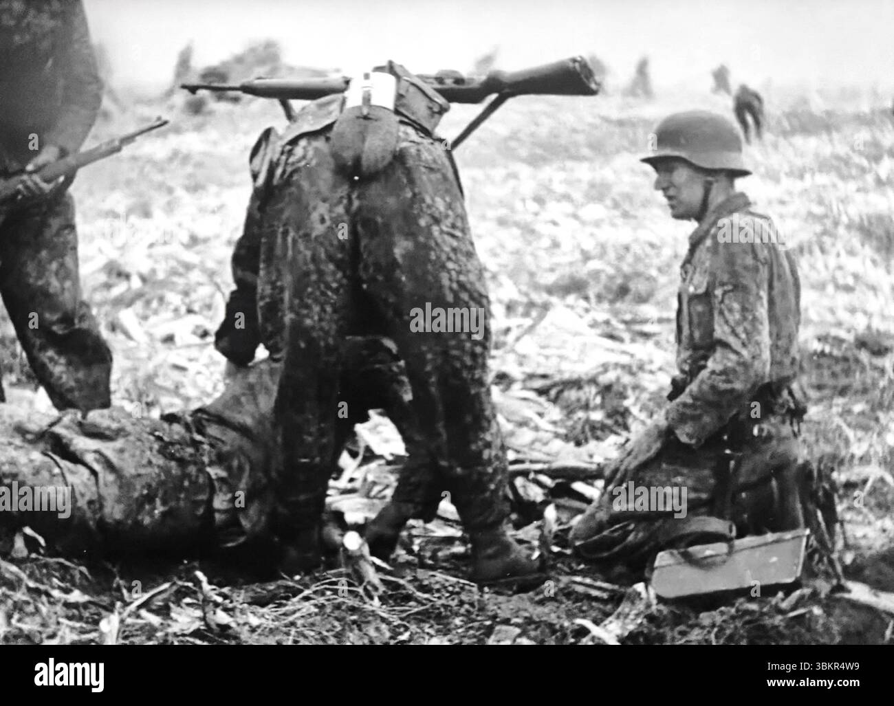 WW2 Bildschirm Schwarzweiß still. Waffen-SS-Soldaten in Pea Dot Camo kümmern sich um einen verwundeten Kameraden an der Ostfront 1944 Stockfoto