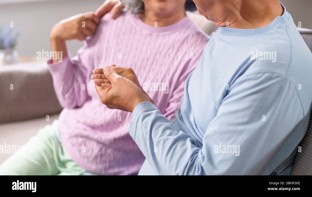 Eine intime Aufnahme eines älteren asiatischen Paares zu Hause. Die zärtliche Handhaltung zeigt Liebe, Unterstützung und dauerhaftes Engagement. Ideal für Ruhestandsthemen oder Stockfoto