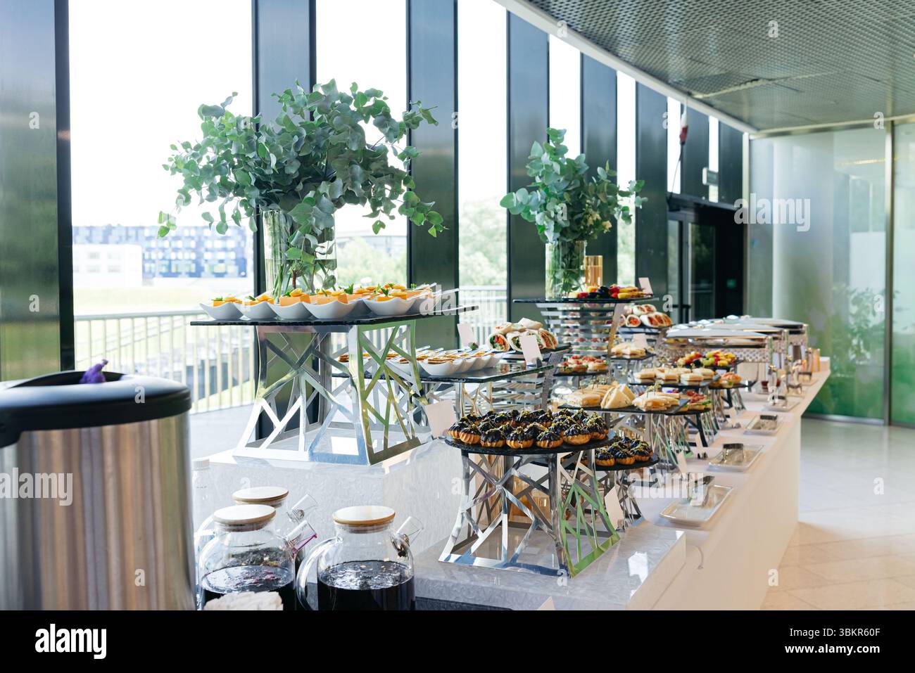 Stilvolles Buffet mit Gourmet-Fingerfood, Desserts und Getränken in einem hellen, modernen Veranstaltungsraum. Stockfoto