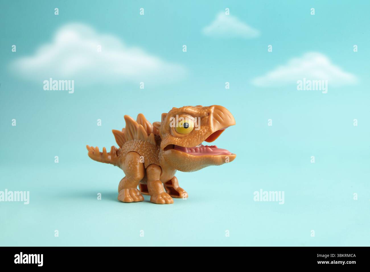 Niedliches und Mini-Plastik-Stiegosaurus-Spielzeug in Aktion auf bewölktem Cyan-Hintergrund Stockfoto