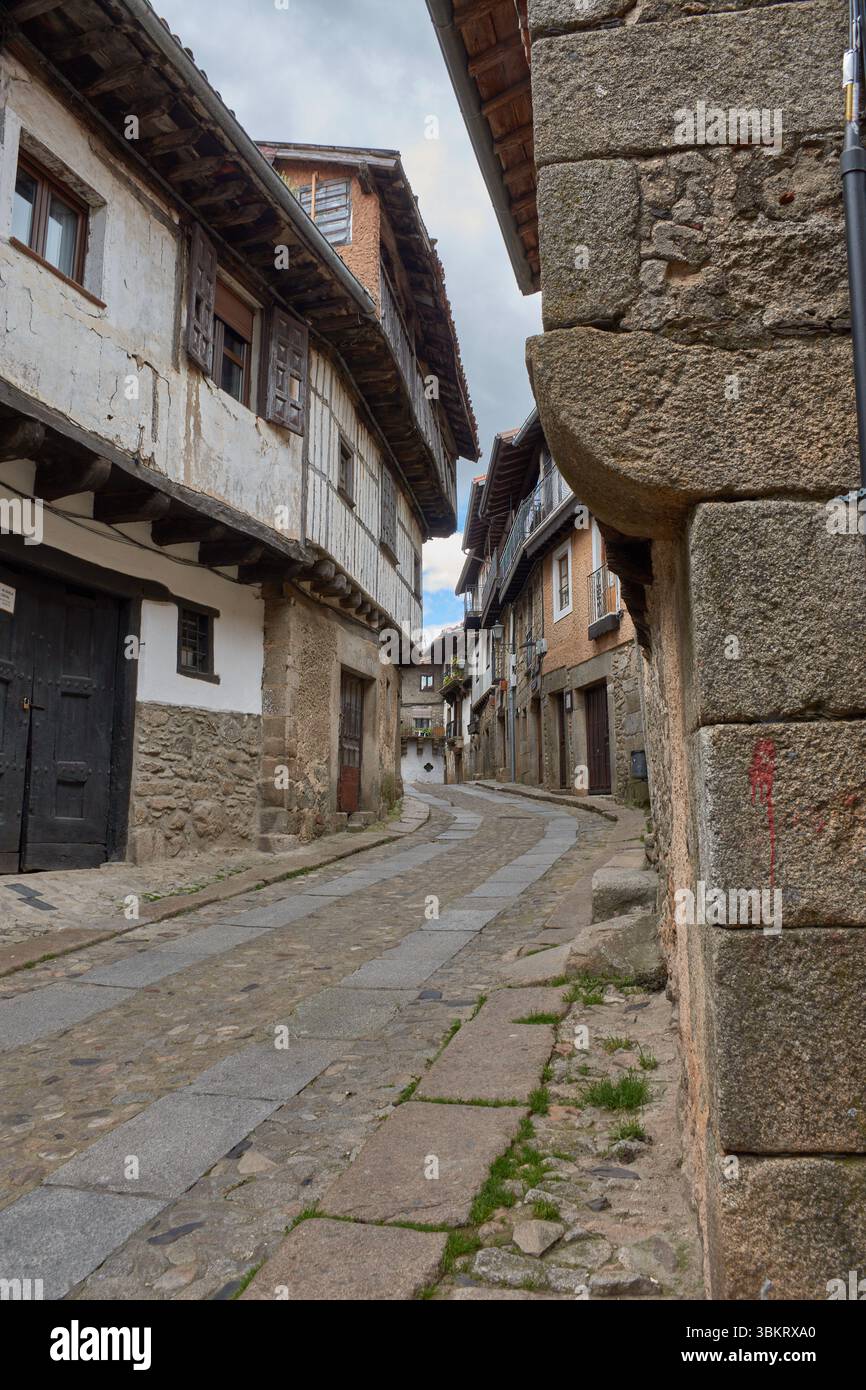 Gepflasterte Gasse in La Alberca, flankiert von traditionellen Stein- und Fachwerkhäusern, mit Balkonen und Fenstern, die mit Töpfen und Blumen dekoriert sind. Stockfoto