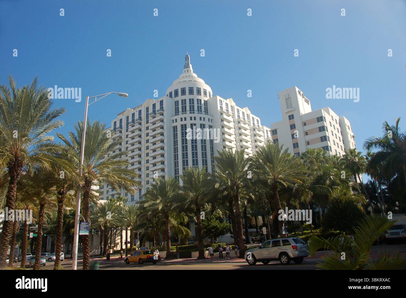 Eleganter weißer Art déco-Wolkenkratzer mit Palmen vor dem Hotel, unter einem klaren blauen Himmel in Miami Beach, Florida, von einem Straßenblick erfasst Stockfoto