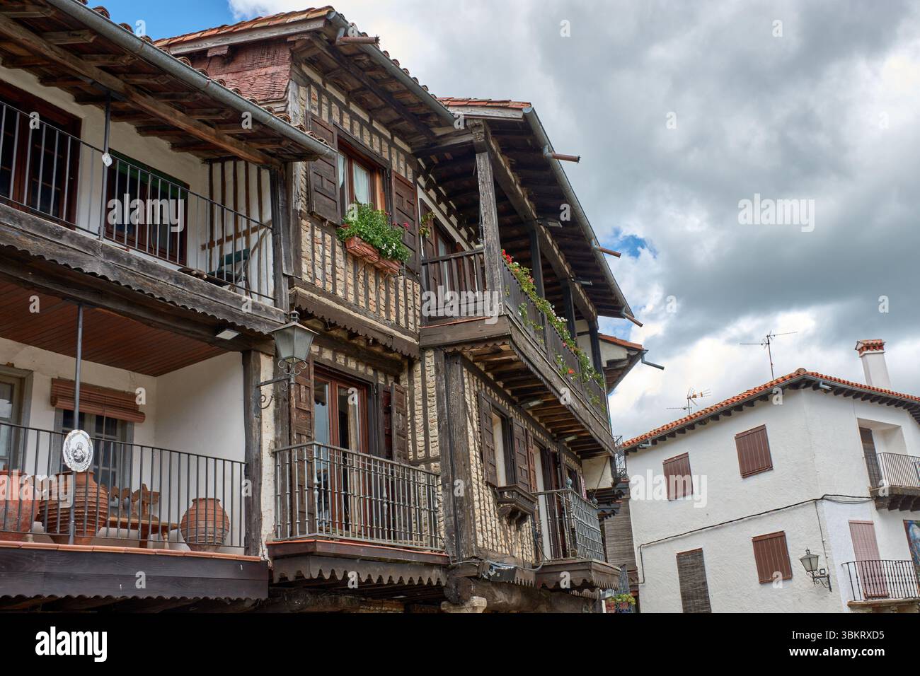 Gepflasterte Gasse in La Alberca, flankiert von traditionellen Stein- und Fachwerkhäusern, mit Balkonen und Fenstern, die mit Töpfen und Blumen dekoriert sind. Stockfoto