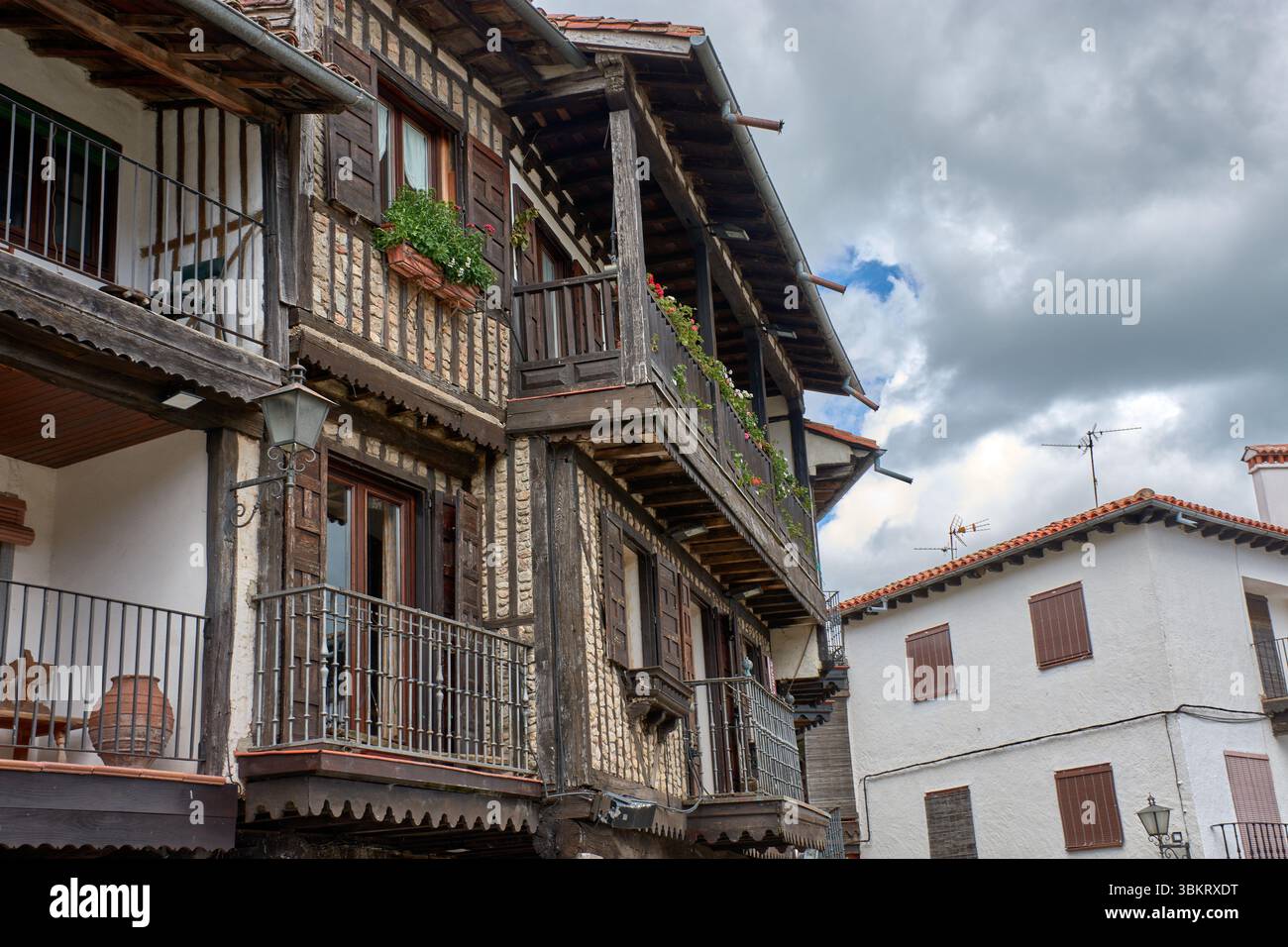 Gepflasterte Gasse in La Alberca, flankiert von traditionellen Stein- und Fachwerkhäusern, mit Balkonen und Fenstern, die mit Töpfen und Blumen dekoriert sind. Stockfoto
