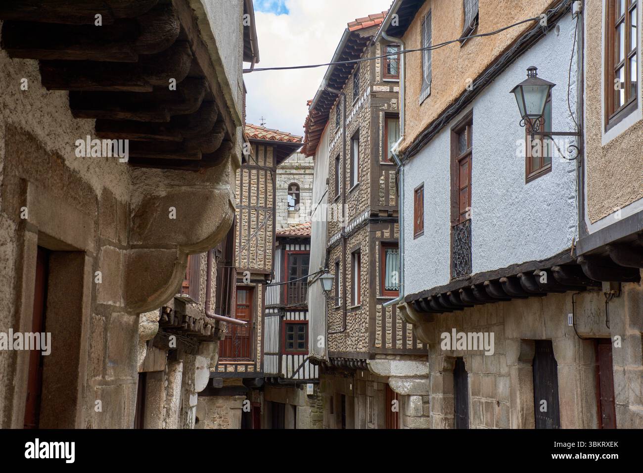Gepflasterte Gasse in La Alberca, flankiert von traditionellen Stein- und Fachwerkhäusern, mit Balkonen und Fenstern, die mit Töpfen und Blumen dekoriert sind. Stockfoto