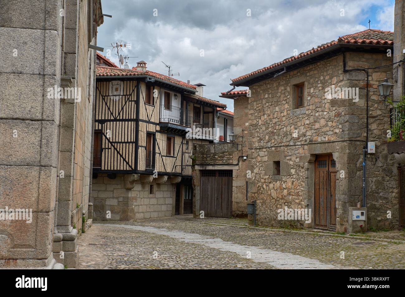 Gepflasterte Gasse in La Alberca, flankiert von traditionellen Stein- und Fachwerkhäusern, mit Balkonen und Fenstern, die mit Töpfen und Blumen dekoriert sind. Stockfoto