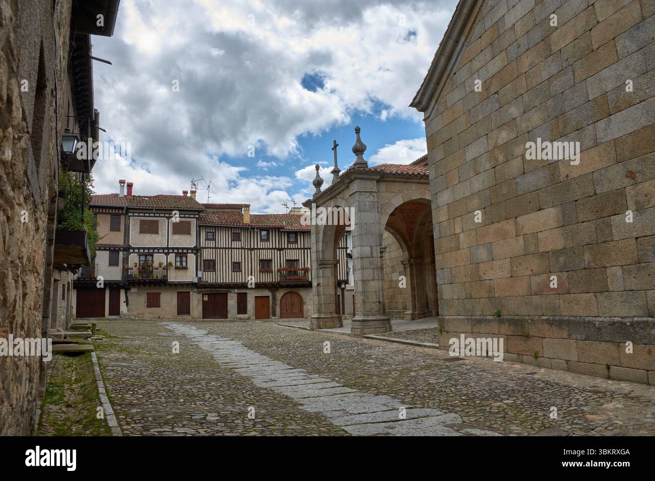 Gepflasterte Gasse in La Alberca, flankiert von traditionellen Stein- und Fachwerkhäusern, mit Balkonen und Fenstern, die mit Töpfen und Blumen dekoriert sind. Stockfoto