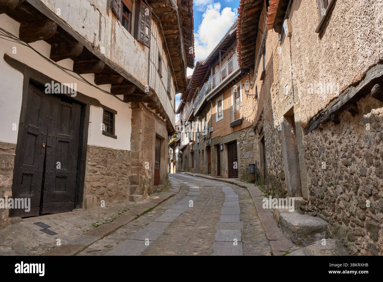 Gepflasterte Gasse in La Alberca, flankiert von traditionellen Stein- und Fachwerkhäusern, mit Balkonen und Fenstern, die mit Töpfen und Blumen dekoriert sind. Stockfoto