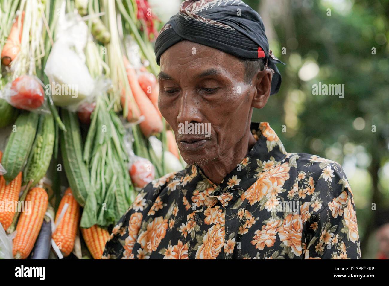 Ein älterer Mann in javanischer Kleidung steht in der Nähe eines traditionellen Gunungans während des Kirab Budaya Ngabean 2024 in Zentral-Java, Indonesien. Stockfoto