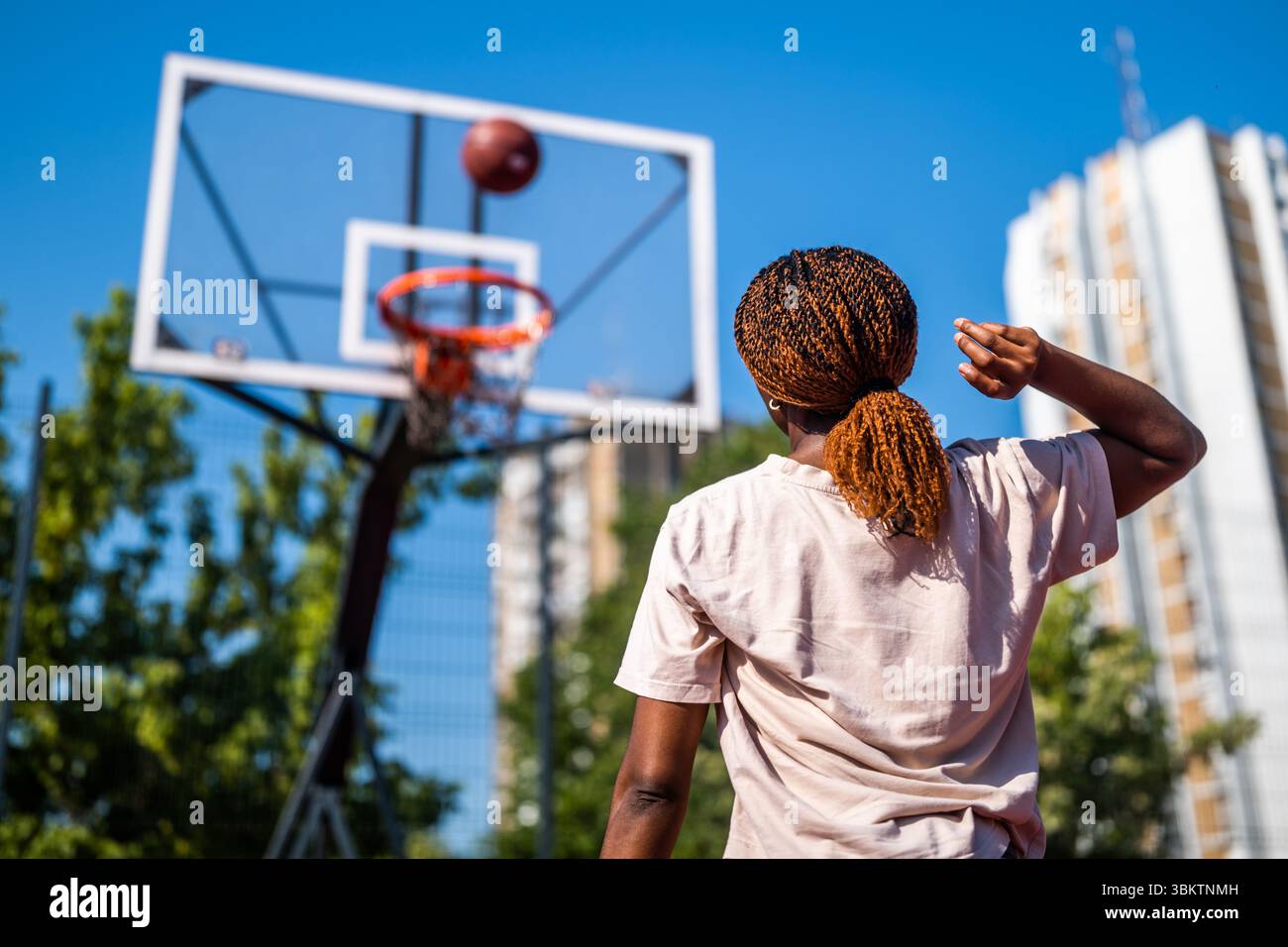 Junge Frau, die morgens alleine Basketball auf dem Sportplatz übt. Sie schießt auf Korb. Stockfoto