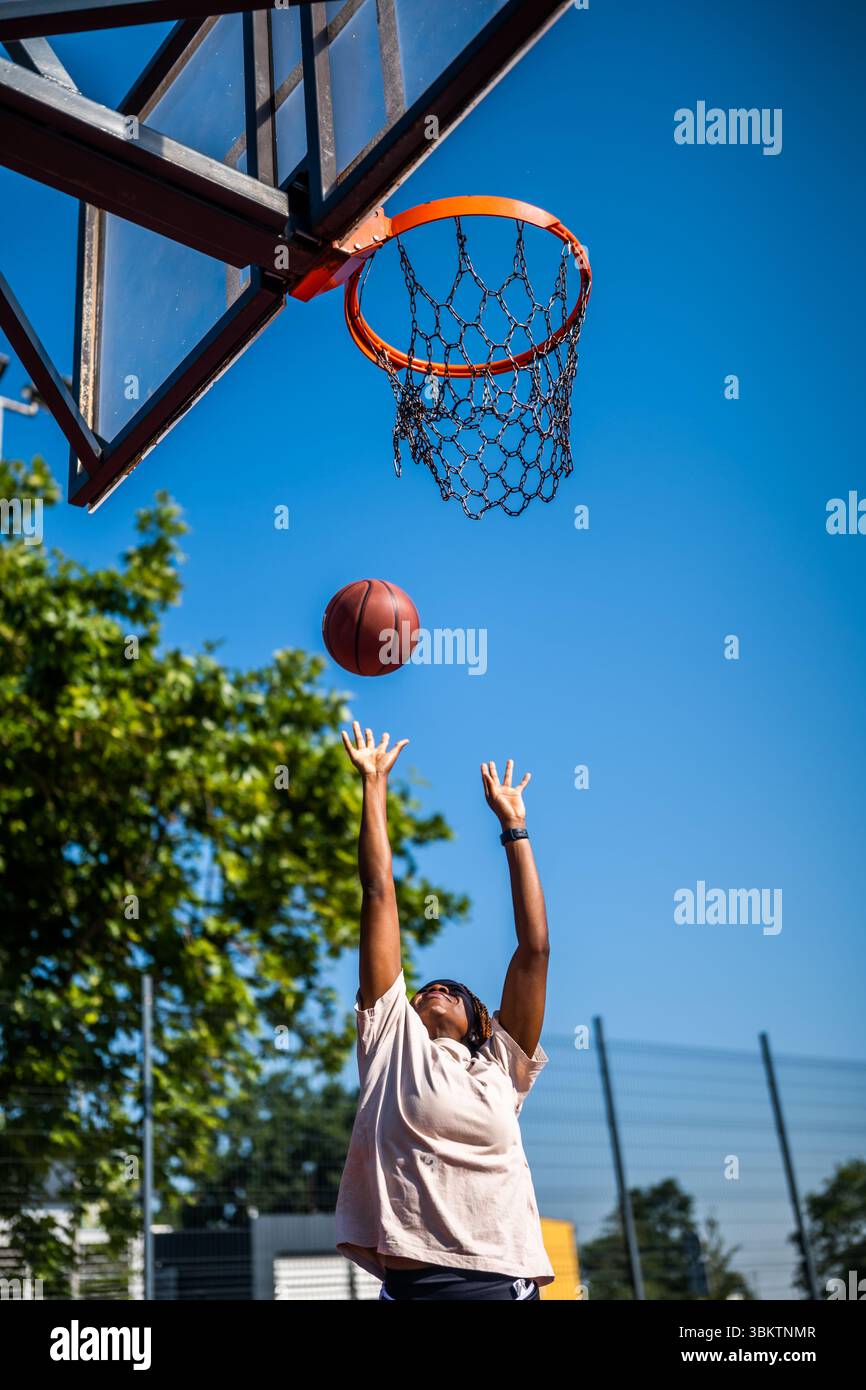 Junge Frau, die morgens alleine Basketball auf dem Sportplatz übt. Sie schießt auf Korb. Stockfoto