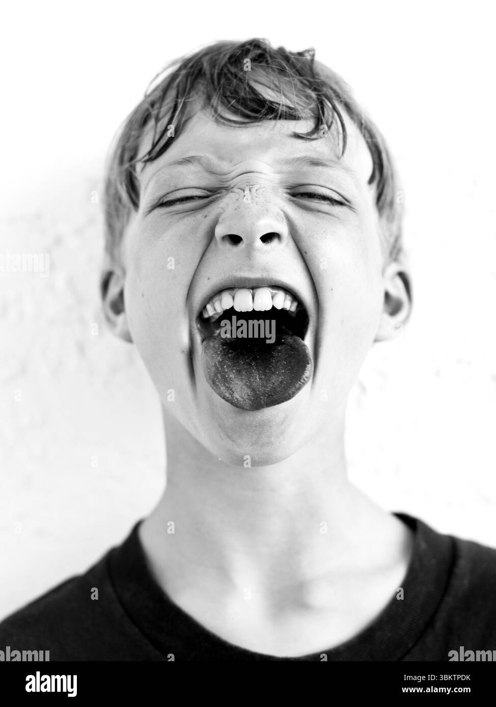 Ein Junge streckt seine Zunge heraus, nachdem er das rote Eis fertig hat. Stockfoto Ein Junge streckt seine Zunge heraus, nachdem er das rote Eis fertig hat. Stockfoto