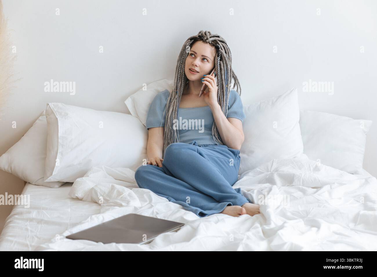 Junge Frau, die am Telefon im weißen Bett spricht. Stockfoto