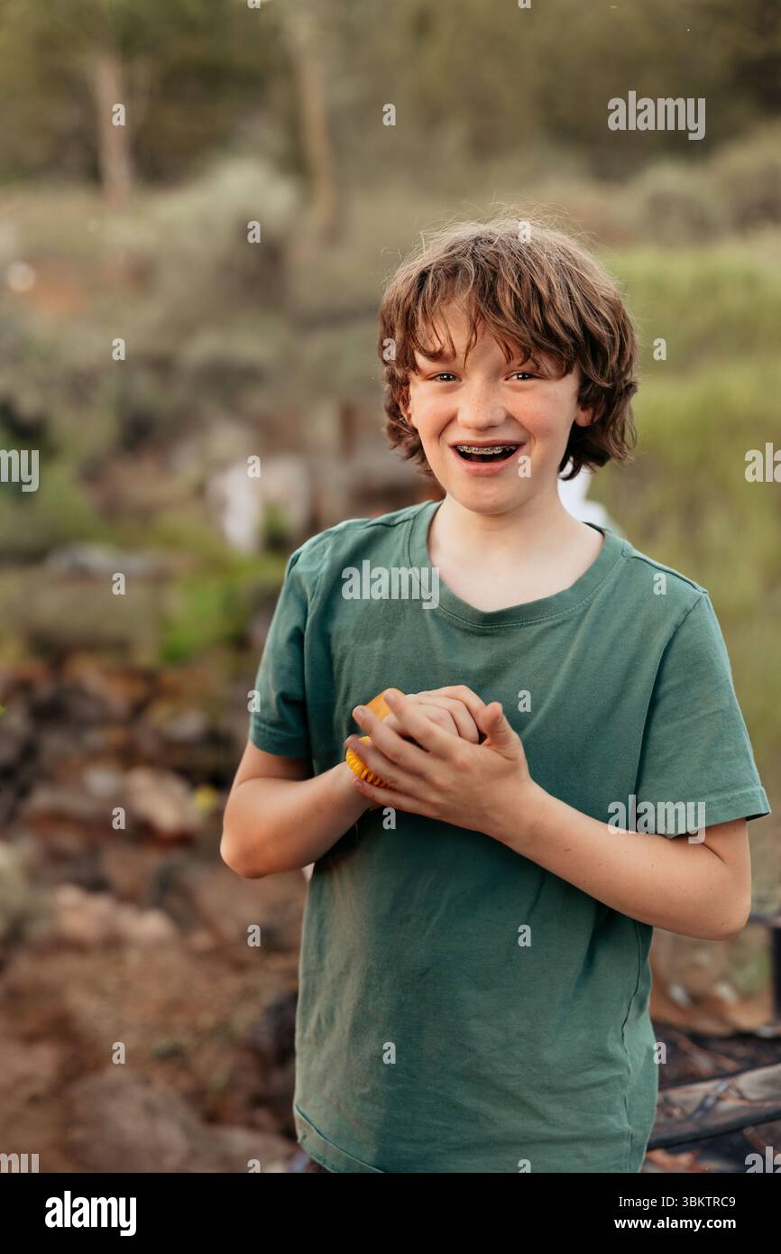 Ein lächelnder Junge draußen mit gefalteten Händen und sichtbaren Zahnspangen Stockfoto