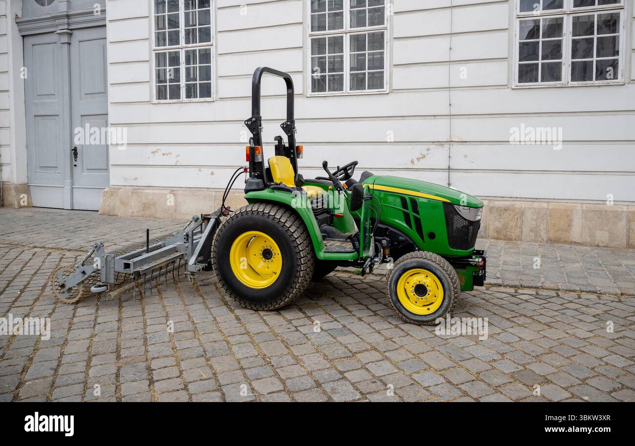 Grüner landwirtschaftlicher Traktor mit angebauter Ausrüstung mit gelben Rädern, die auf einer Kopfsteinpflasterstraße geparkt sind Stockfoto