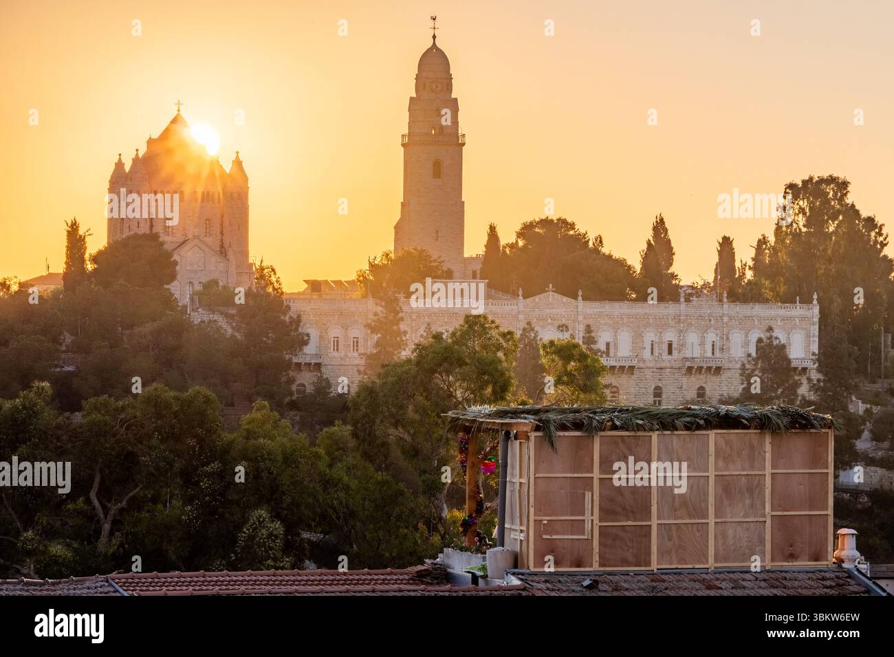 Während des jüdischen Feiertags von Sukkot geht die Sonne hinter der Dormitio Abbey und der Altstadt von Jerusalem in Israel auf, mit einer Sukkkah im Vordergrund Stockfoto