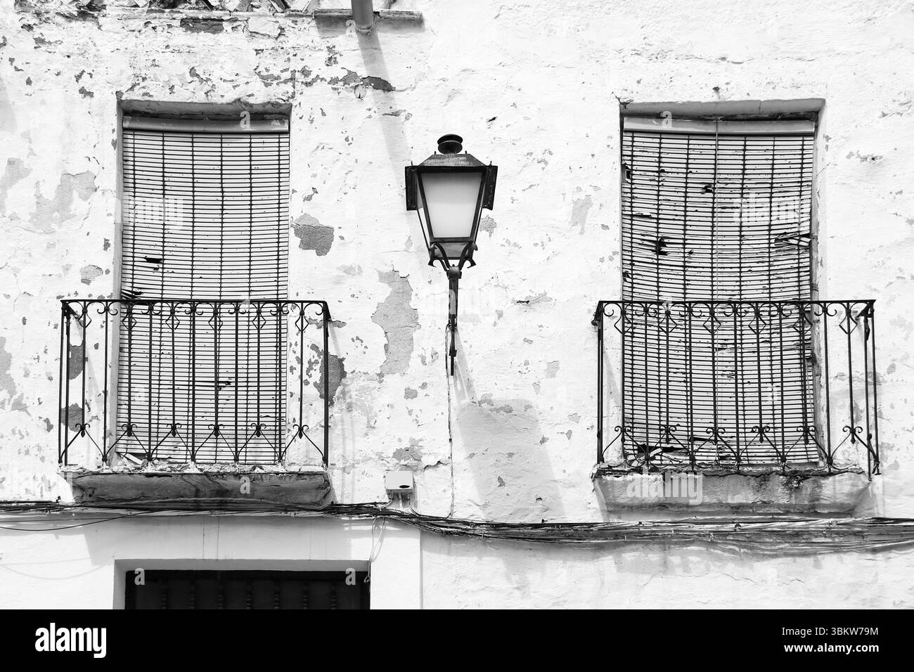 Abgesplittete Fassade mit schmiedeeisernen Balkonen und Vintage Straßenlaterne in Villanueva de los Infantes, Ciudad Real, Spanien Stockfoto