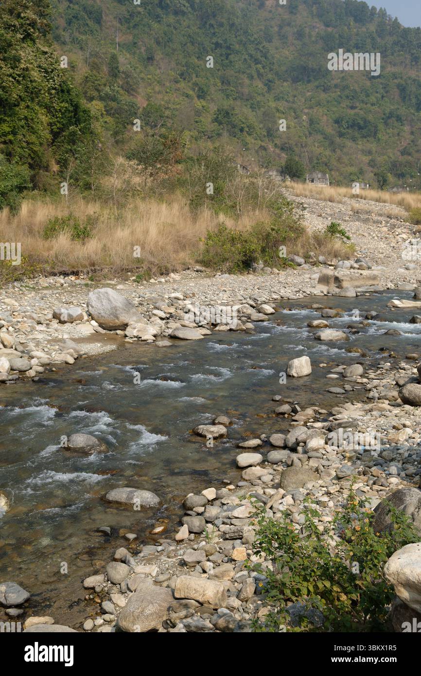 Wasser fließt über Felsen in einem trockenen Flussbett, eine Lebensader durch die Landschaft aus trockenem Gras und bewaldeten Hügeln. Stockfoto