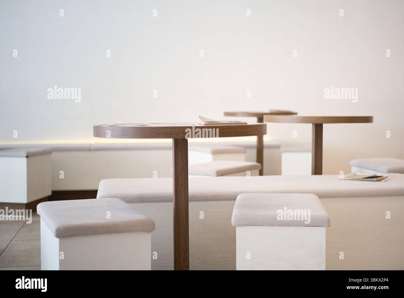 Minimalistisches Café-Interieur mit runden Holztischen, weichen Sitzgelegenheiten und Tageslicht in einem ruhigen Raum. Stockfoto