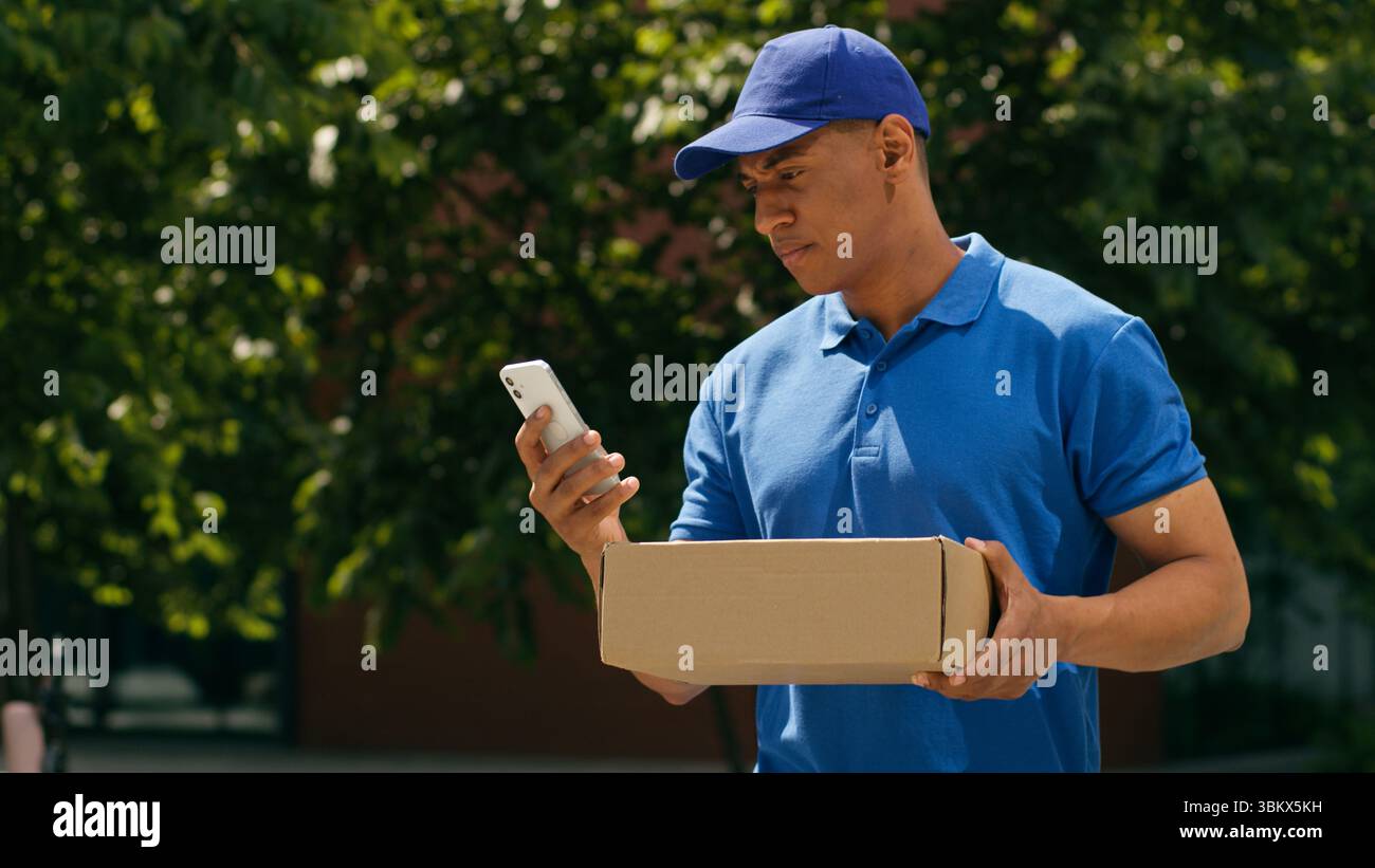 Kleinunternehmen Konzept afroamerikanischer Kurier Mann sucht Adresse mit Handy-App zu Fuß in der Stadt Zustellungsmann männliche Post Service E-Commerce Stockfoto