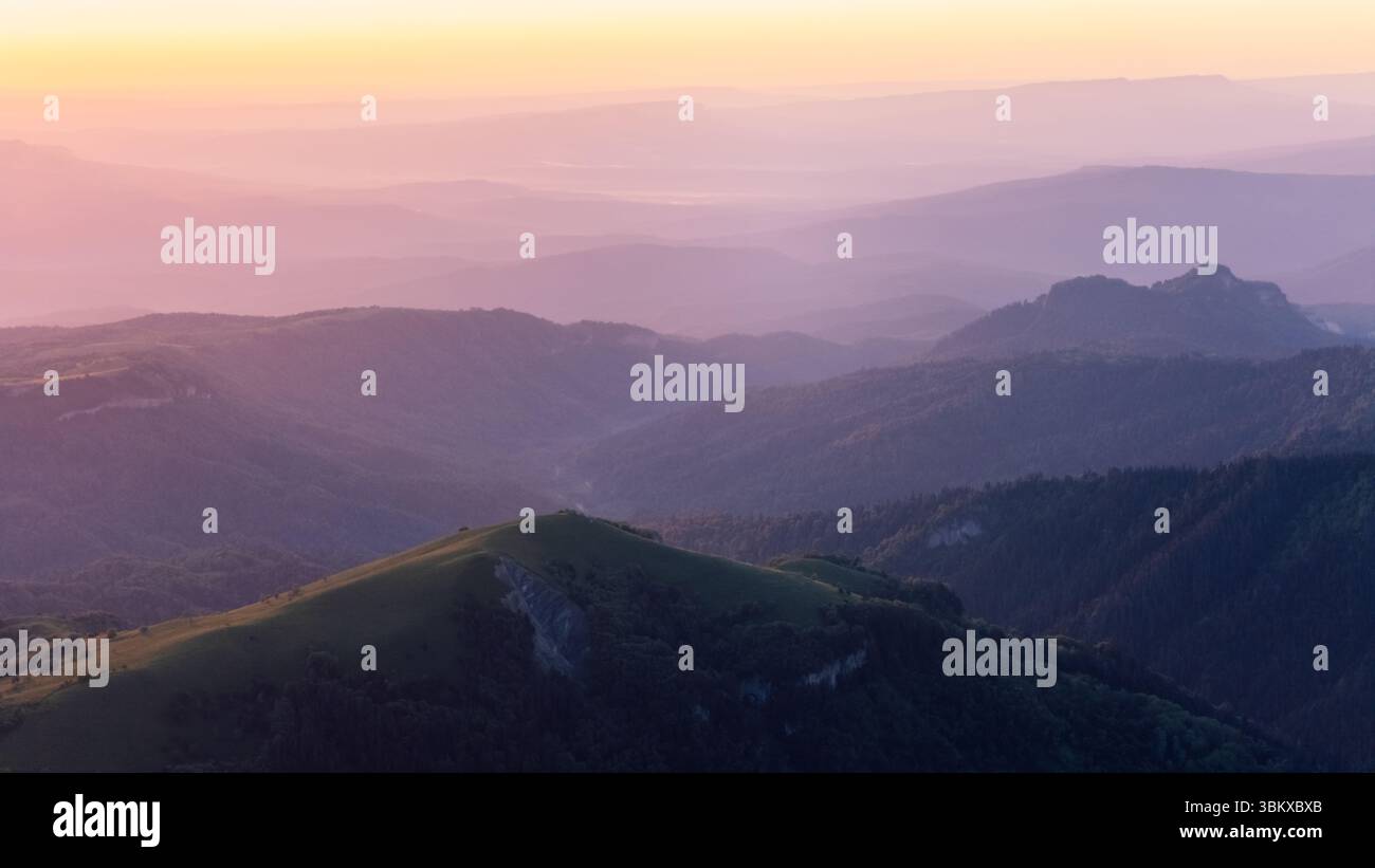 Friedliche Berglandschaft bei Sonnenaufgang mit bunten Nebelschichten und sanftem goldenem Licht. Stockfoto