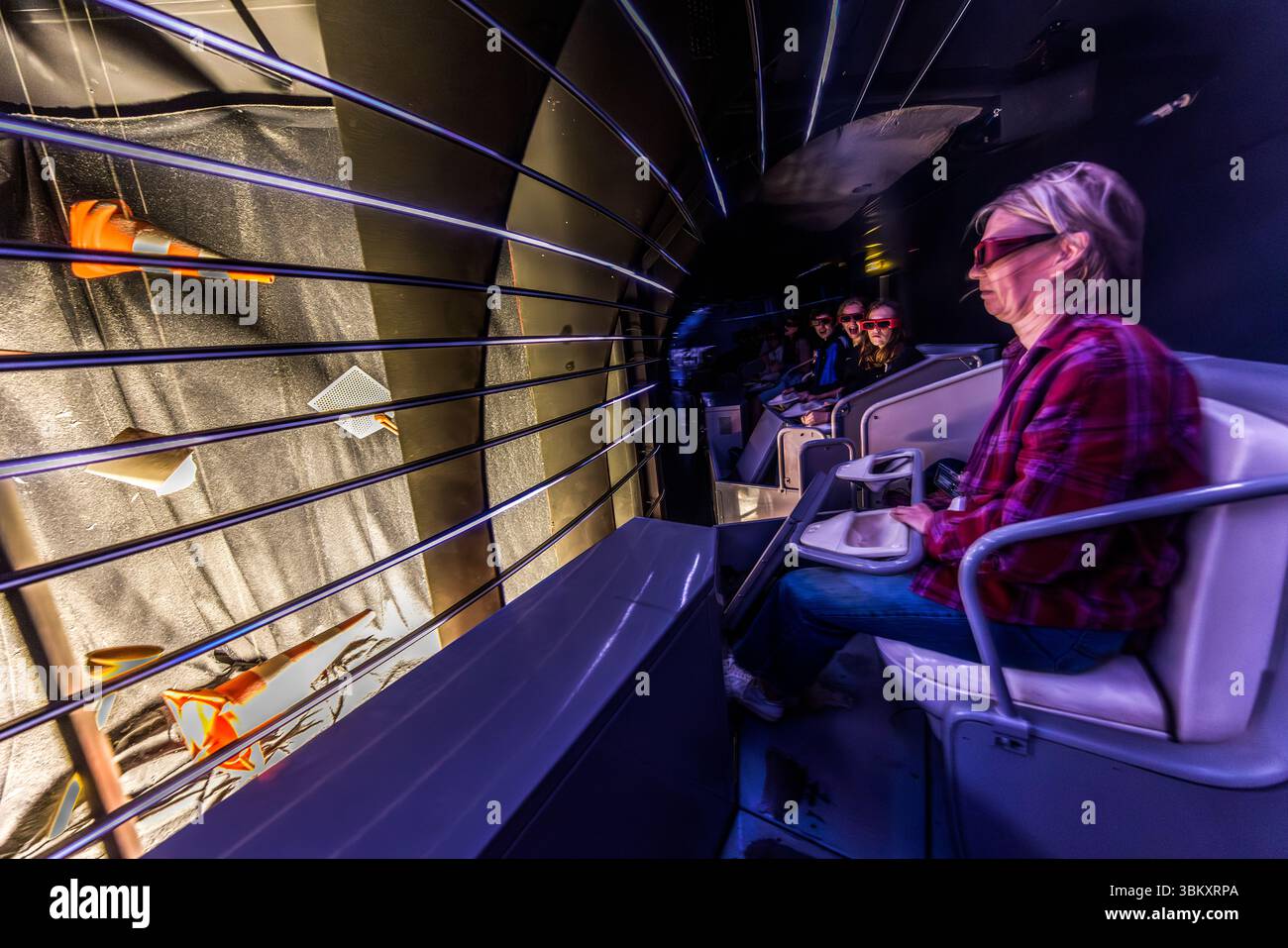 Besucher sitzen auf weißen Schalensitzen im Fahrzeug und sehen sich im Freizeitpark Futuroscope eine dynamische Filmshow durch eine 3D-Brille an. Die Attraktion kombiniert physische Bewegung mit dreidimensionaler Filmprojektion. 1987 war Futuroscope der erste Freizeitpark in Europa, der diese Art von Attraktion zeigte. Das Futuroscope bei Poitiers ist ein Vergnügungspark, der sich auf futuristische Themen, Multimedia-Erlebnisse und innovative Attraktionen spezialisiert hat. Avenue René Monory, Chasseneuil-du-Poitou, Vienne, Nouvelle-Aquitaine, Frankreich Stockfoto