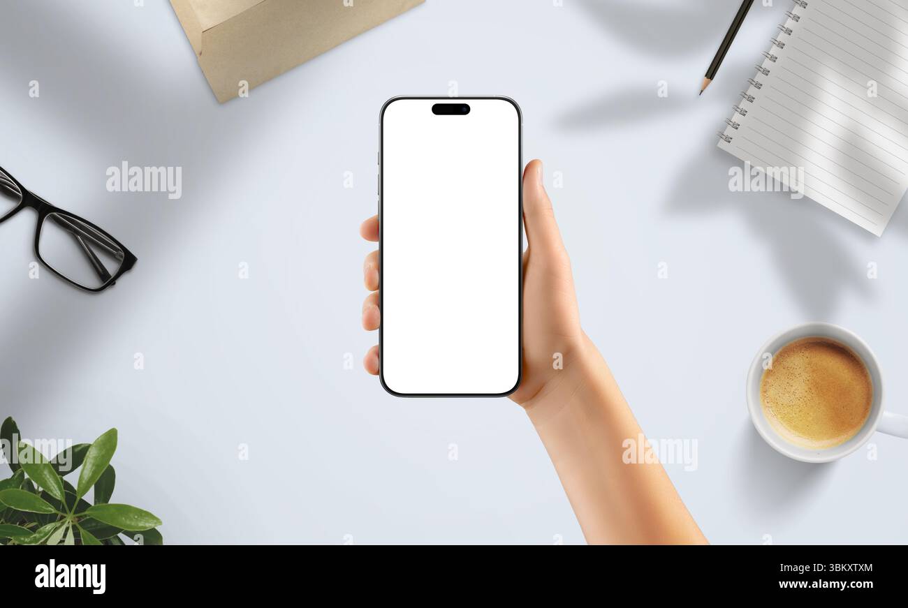 Smartphone mit leerem Bildschirm im kreativen Arbeitsbereich. Umgeben von Kaffee, Notizbuch, Gläsern und weichen natürlichen Schatten Stockfoto