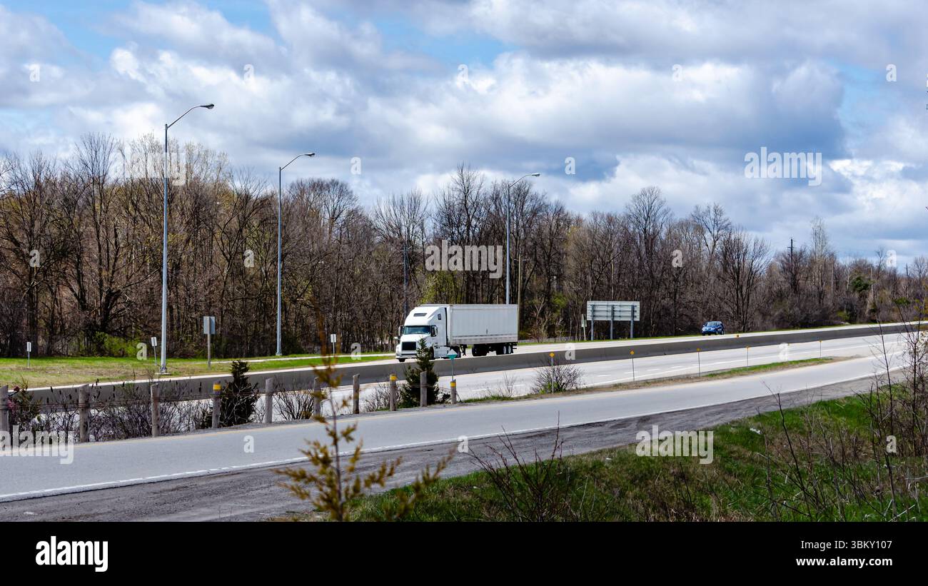 Einsamer Transportwagen und Auto auf einer Autobahn im Frühling unter bewölktem Himmel. Stockfoto