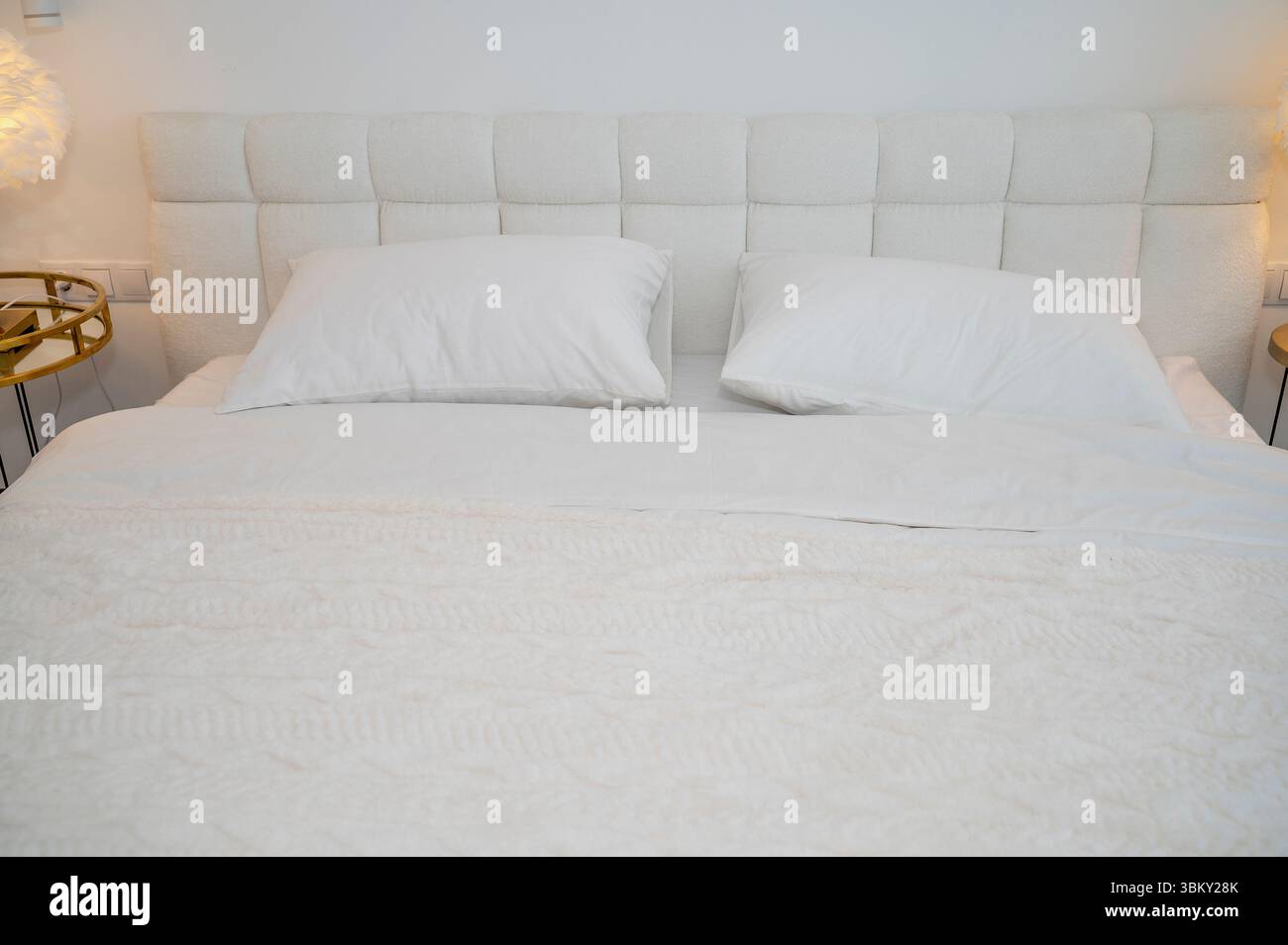 Ein gemütliches, modernes Hotelzimmer mit einem ordentlich gefertigten weißen Bett. Das Zimmer ist in minimalistischem Stil eingerichtet Stockfoto