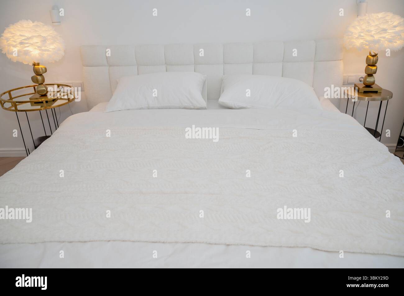 Ein gemütliches, modernes Hotelzimmer mit einem ordentlich gefertigten weißen Bett. Das Zimmer ist in minimalistischem Stil eingerichtet Stockfoto