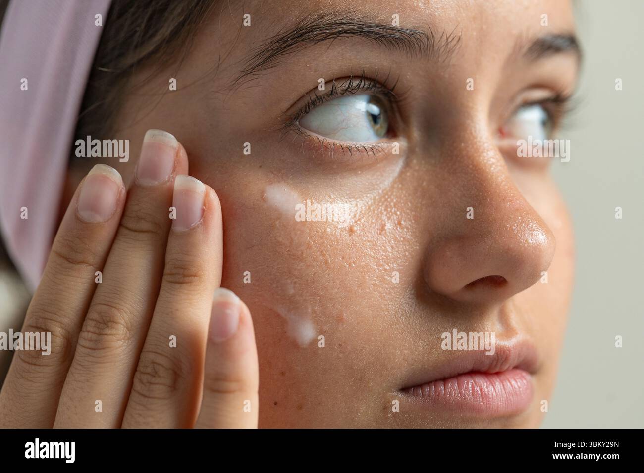 Eine dermatologische Makroaufnahme, bei der eine Frau eine Creme aufträgt, um die zarte Haut unter ihren Augen zu behandeln Stockfoto