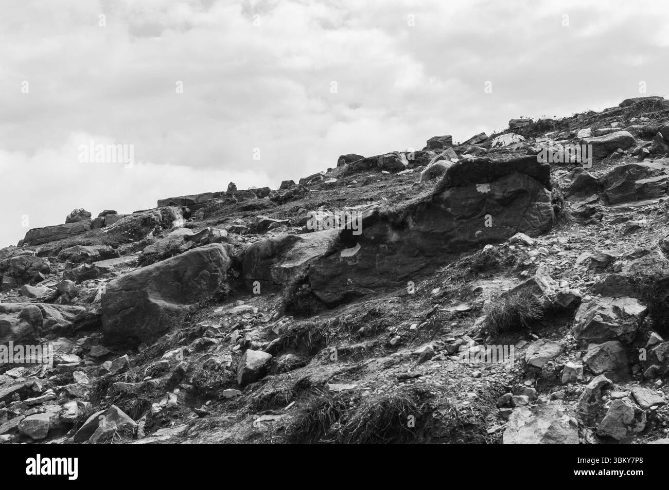 Ein felsiger Hügel mit einem bewölkten Himmel im Hintergrund. Die Felsen sind verstreut und der Hügel ist steil Stockfoto
