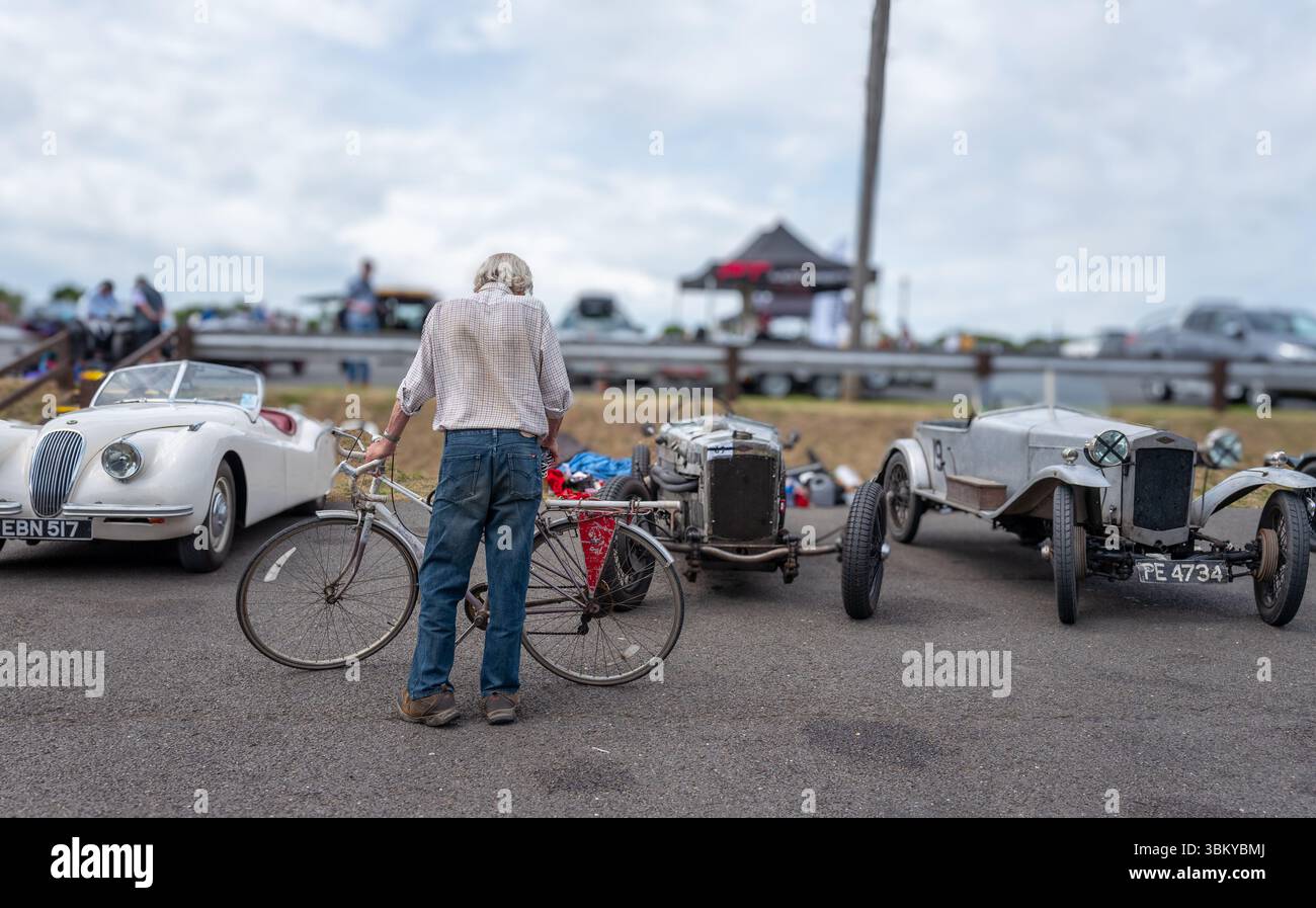 Ein Mann mit einem Fahrrad, der eine Reihe von Oldtimern aus der Vorkriegszeit im Fahrerlager bei einem Oldtimer-Motorrennen-Treffen sucht. Stockfoto