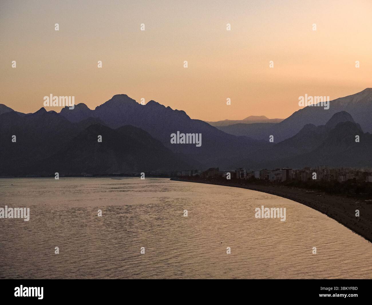 Eine malerische Aussicht auf Antalya, Türkei, mit Blick auf die Küste der Stadt und das Taurusgebirge im Hintergrund bei Sonnenuntergang oder Sonnenaufgang, die die natürliche Schönheit und die urbane Landschaft der Region unterstreicht. Stockfoto