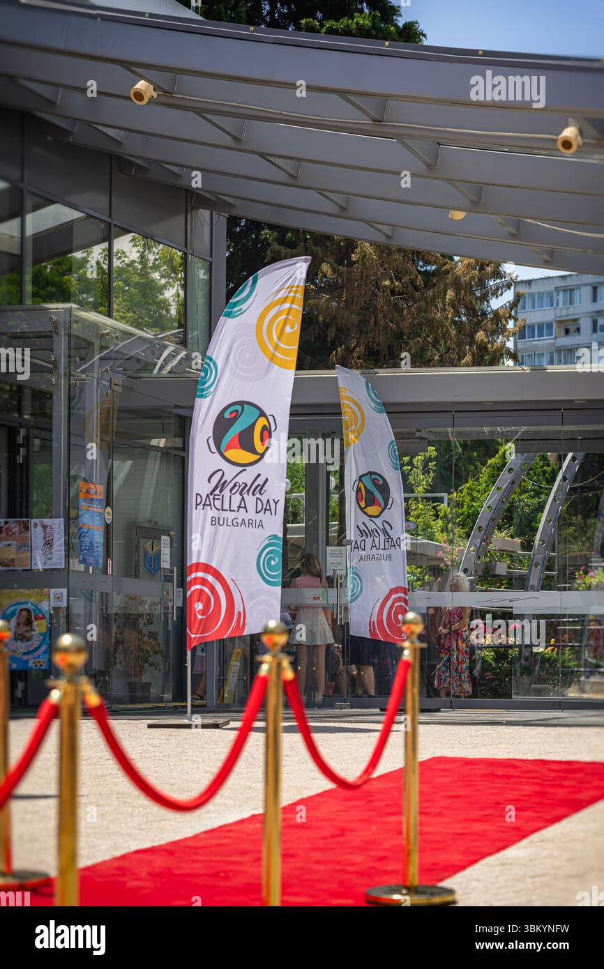 Eintritt zum World Paella Day Festival in Burgas, Bulgarien, mit rotem Teppich und Markenflaggen, die Gäste zu kulinarischen Feierlichkeiten einladen. Konzept des Ereignisses Stockfoto