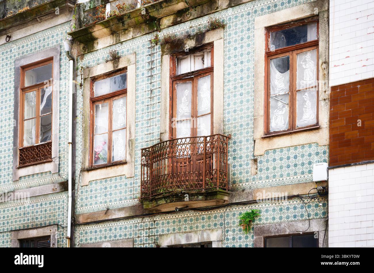 Verwitterte Eleganz und verblasster Glanz an der Fassade des alten Gebäudes mit traditionellen Azulejo-Fliesen, verwitterten Holzfenstern und einem rostigen Balkon in der Altstadt Stockfoto