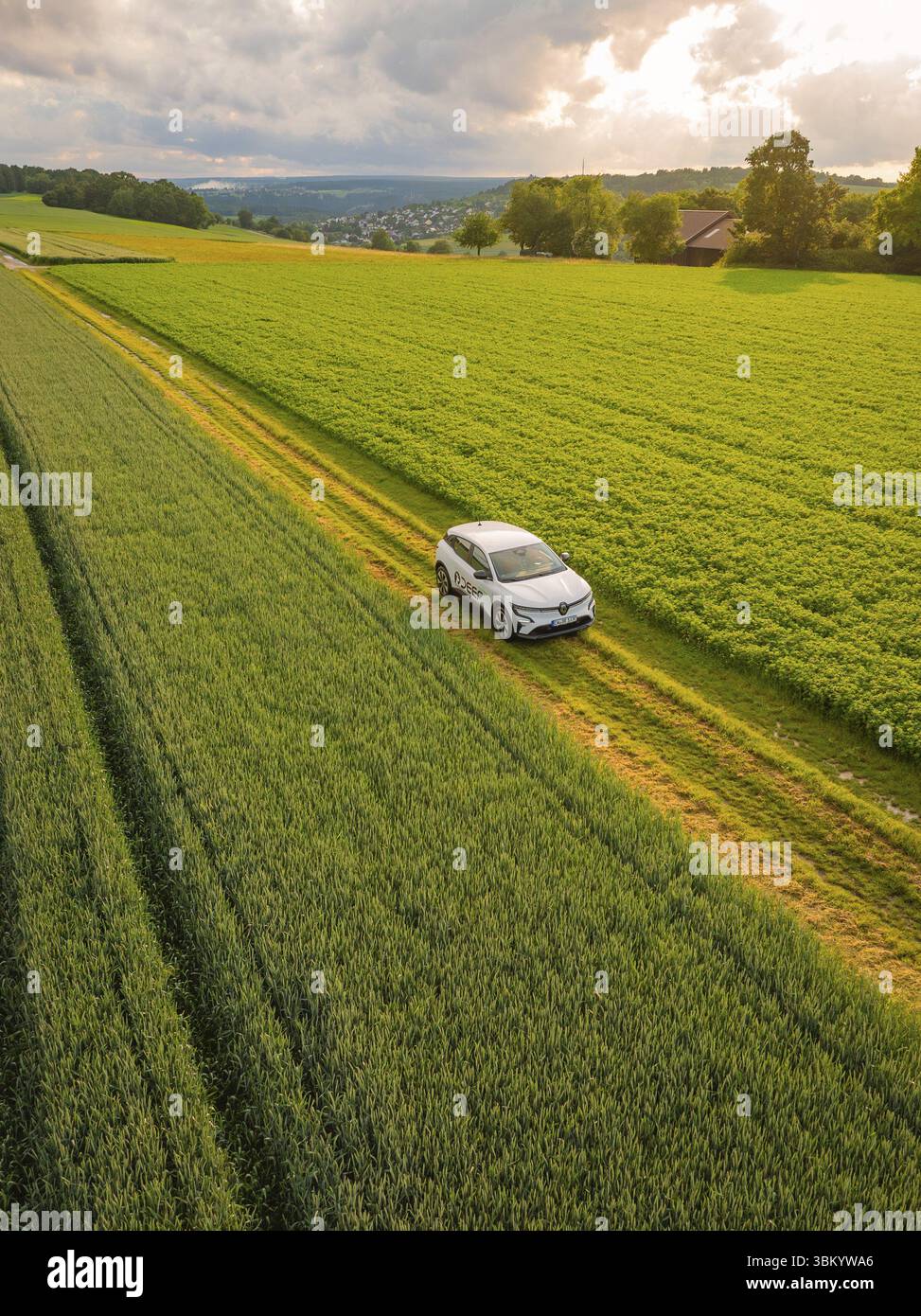 Ein Auto fährt auf einer Landstraße durch grüne Felder, ein Dorf im Hintergrund, Deer E- Carsharing, Renault Megane Elektroauto, Calw, Schwarzwald, G Stockfoto