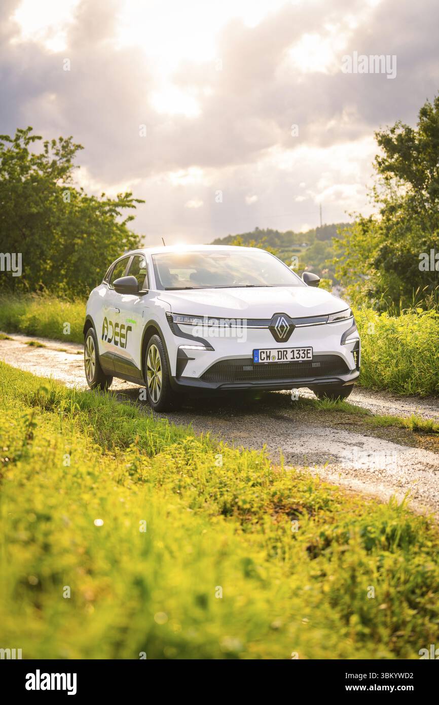Weißes Auto auf einer Landstraße mit grünen Wiesen und bewölktem Himmel im Hintergrund, Deer E- Carsharing, Renault Megane Elektroauto, Calw, Schwarzwald, GE Stockfoto