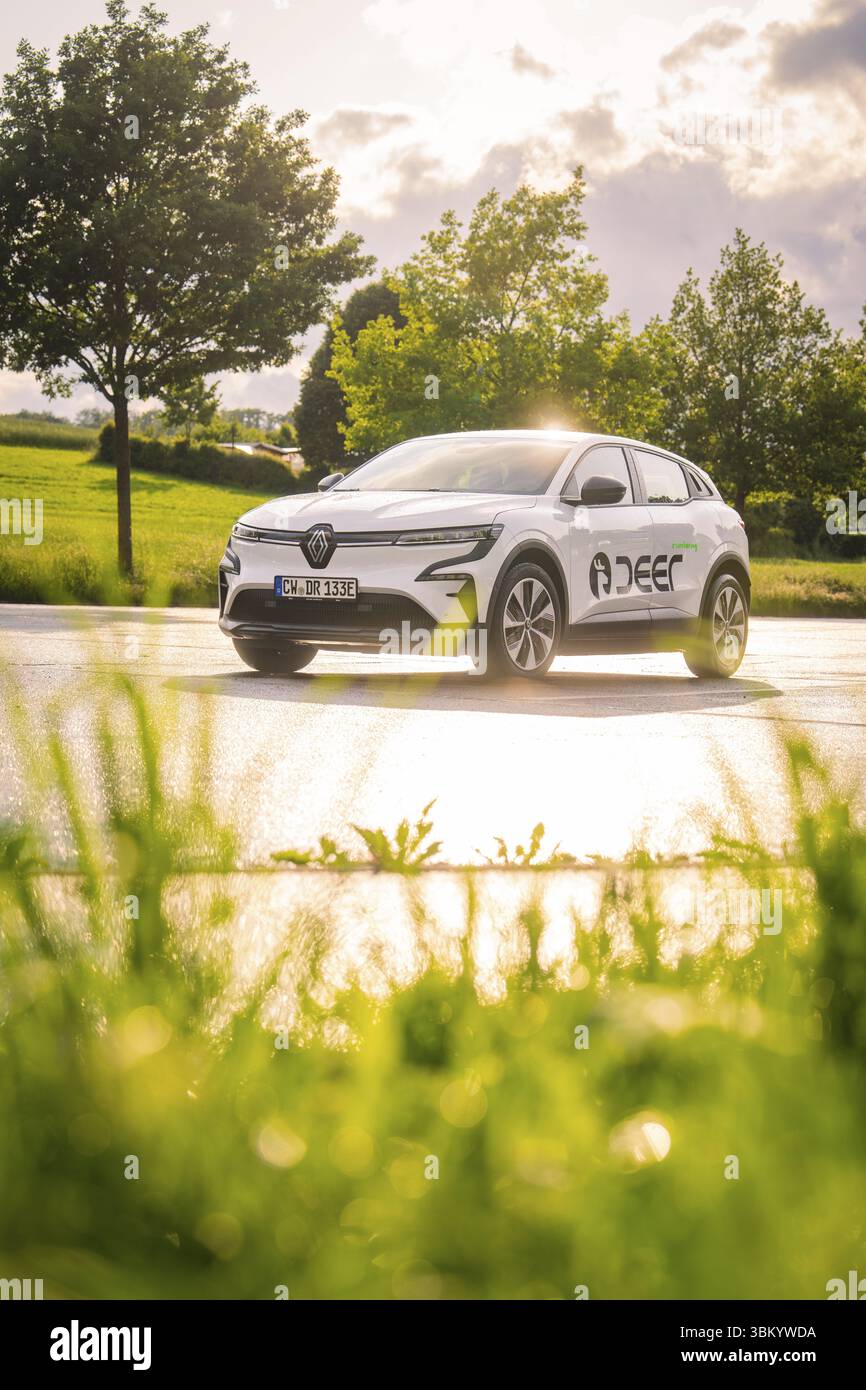 Weißes Auto auf nasser Straße, reflektierende Sonnenstrahlen, ländliche Umgebung, Hirsch E-Carsharing, Renault Megane Elektroauto, Calw, Schwarzwald, Deutschland, Europa Stockfoto