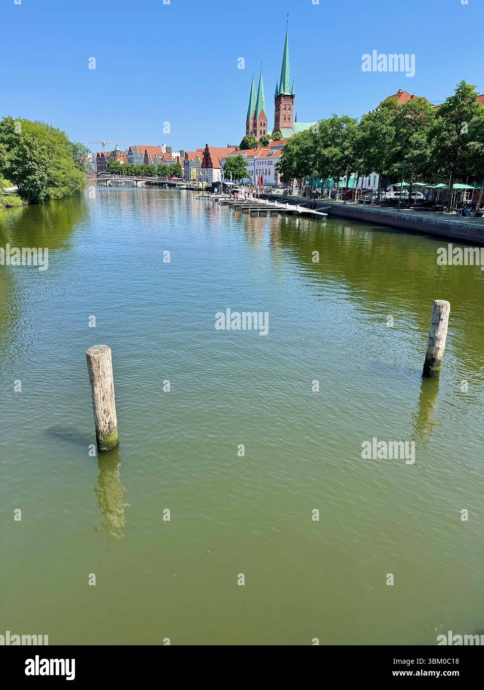 Blick auf die Trave mit den Zwillingstürmen des Lübecker Doms vorbei an Cafés am Ufer in Lübeck, Deutschland. - Smartphone-aufgenommenes Stockfoto