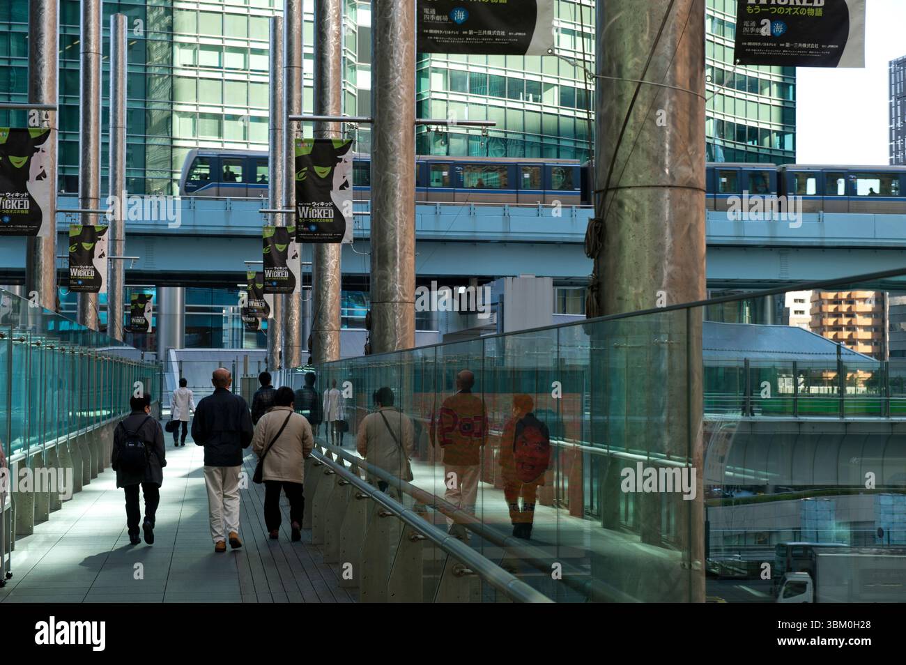 Menschen auf einem erhöhten Gehweg, während die Yurikamome Monorail über den Wolkenkratzern in der Shimbashi Shiodome Gegend von Tokio, Japan, vorbeifährt. Stockfoto