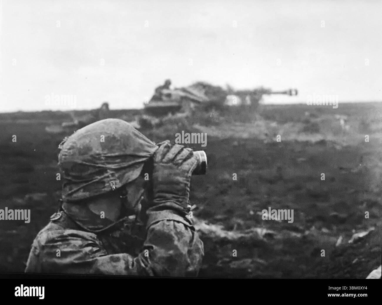WW2 Screen B&W STILL deutscher Waffen SS Soldat in Tarnuniform beobachtet für eine Panzerabwehrkanone an der Ostfront 1944 Stockfoto
