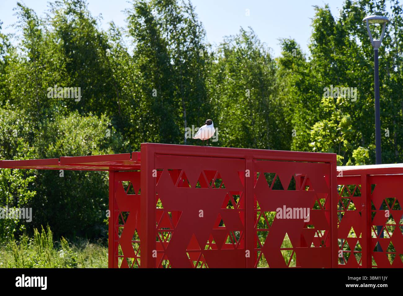 Ein kleiner Vogel thront auf einem roten Gebäude, umgeben von Grün unter hellem Sonnenlicht Stockfoto