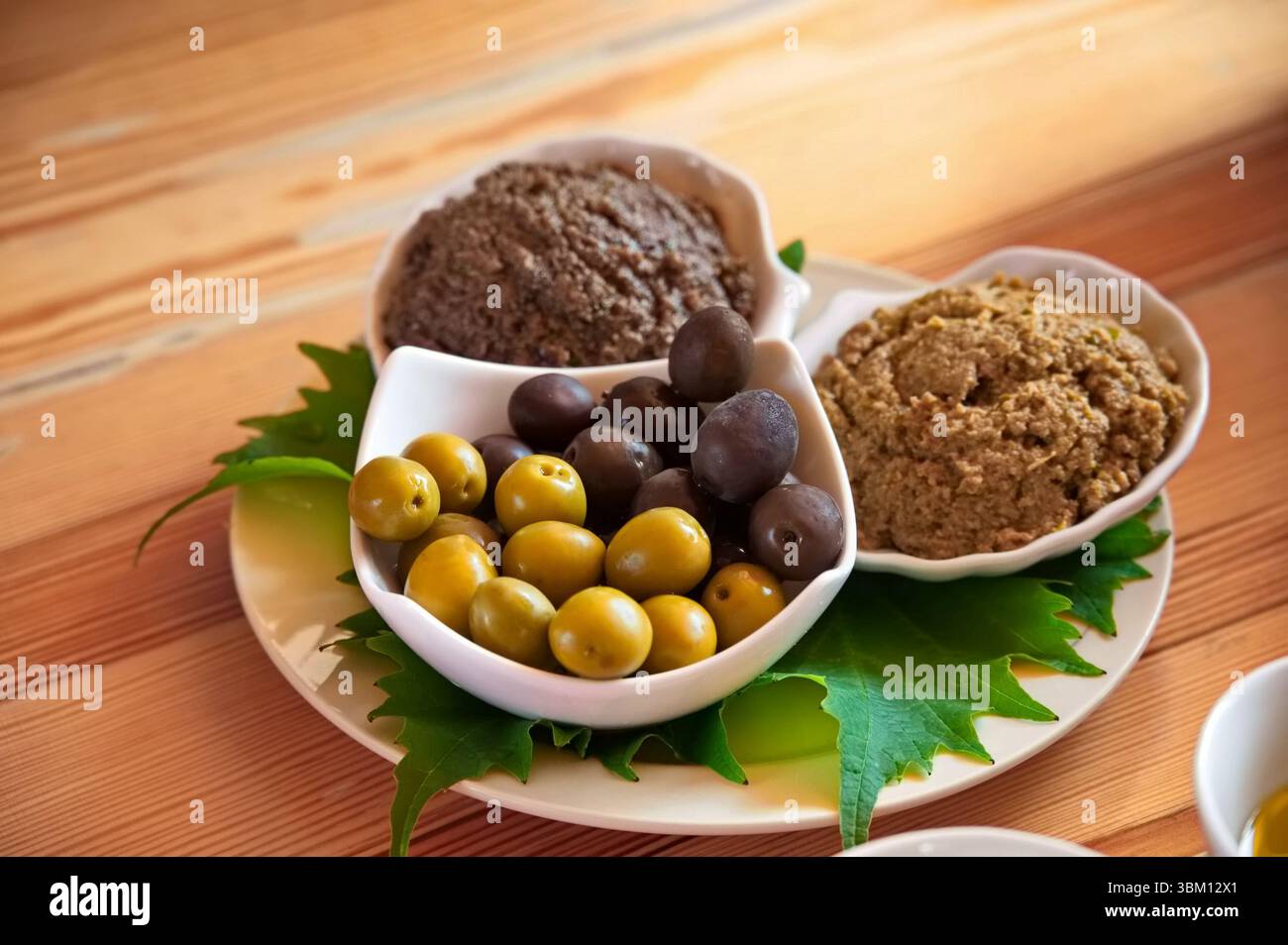 Oliven und Überwürfe auf Olivenbasis auf dem Holztisch Stockfoto